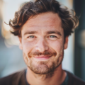 Homme souriant avec barbe et cheveux bouclés.