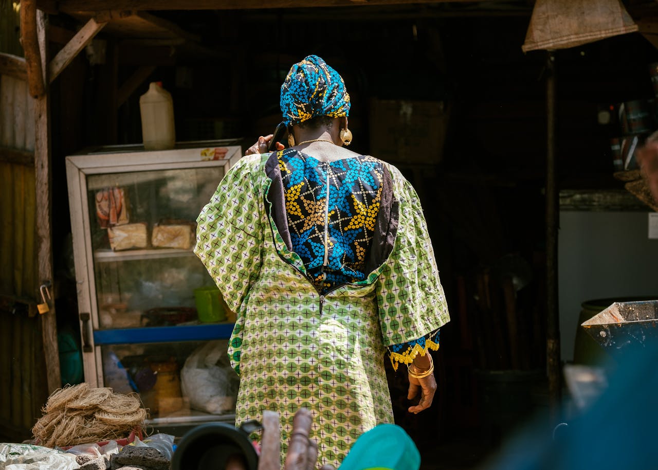 A woman in traditional attire shops at an outdoor market in Tudun Wada, Nigeria.