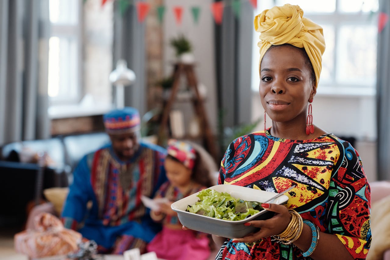 A family in vibrant traditional African clothing celebrating together with African cuisine indoors.